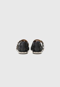 Black leather shoes with a textured pattern, round toe, rear strap, and silver buckle accents. Flat soles with a subtle beige edge.