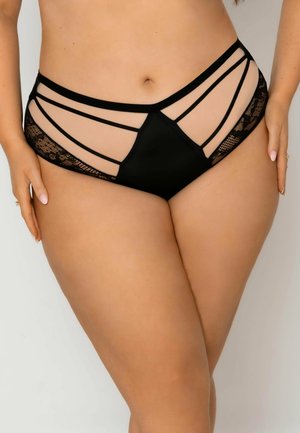 Czarne majtki z wysokim stanem z przezroczystymi panelami, koronkowymi bokami i wieloma cienkimi paskami, noszone przez osobę plus size stojącą z rękami przy biodrach.