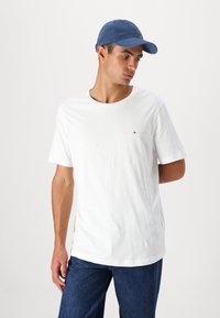 Hvit bomull t-skjorte med kortermet og rund hals, med et lite brodert logo i gull. Kombinert med en blå caps.