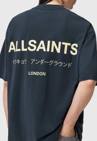 Μαύρο T-shirt με έντονα μπεζ γράμματα: «ALLSAINTS», ιαπωνικούς χαρακτήρες και «LONDON» στην πλάτη. Χαλαρή εφαρμογή, βαμβακερό υλικό.