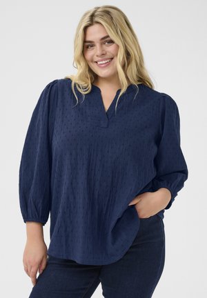 Navy blue, long-sleeve blouse with a v-neck, gathered shoulders, and textured pattern of small dots. Relaxed fit, lightweight fabric.