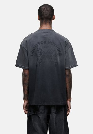 Zwarte oversized t-shirt met een vervaagd ontwerp van vlinders en de tekst "GOOD FOR NOTHING" op de achterkant. Zachte katoen stof.