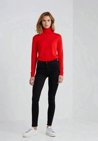 Pulôver vermelho de gola alta, corte ajustado, com mangas longas. Emparelhado com jeans skinny pretos e ténis brancos. Design simples, cores sólidas.