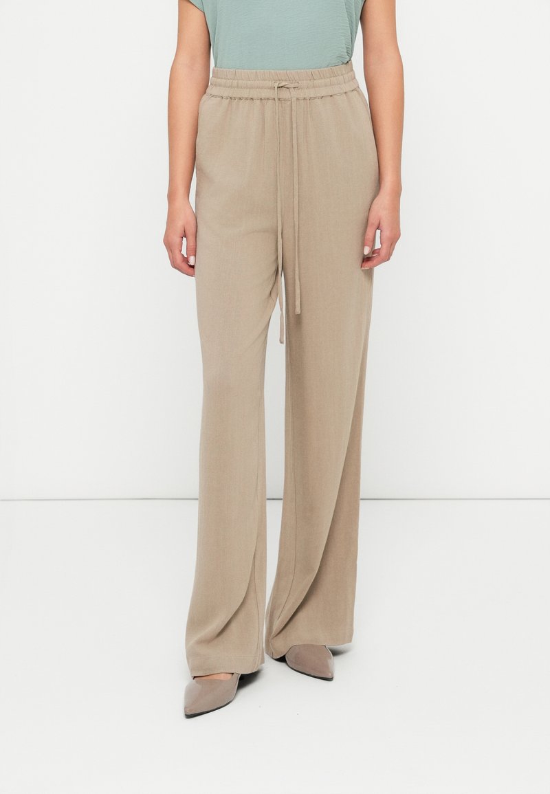 Pantalon large beige avec une taille élastique et une texture douce, associé à un haut vert clair et des ballerines neutres à bout pointu.
