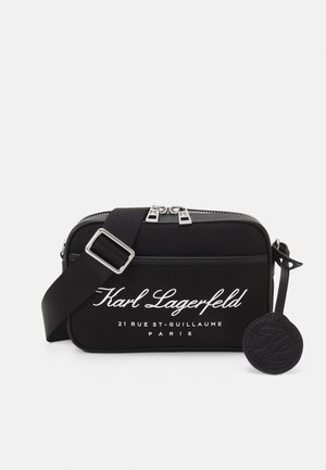 Černá obdélníková taška přes tělo s nastavitelným popruhem, stříbrným zipem, bílým nápisem „Karl Lagerfeld 21 Rue St-Guillaume Paris“ a kulatou značkou s logem.