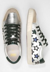 Stříbrné metalické tenisky se zelenými tkaničkami, semišovými detaily a hvězdicovým vzorem. Mají strukturovanou gumovou podrážku a kontrastní patu.