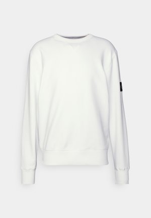 Sweatshirt blanc avec un col rond, des poignets et un ourlet côtelés, présentant un petit logo noir sur la manche gauche. Texture lisse, design décontracté.