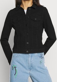 Svart denimjacka med krage, knappstängning fram och två bröstfickor. Figursydd design med långa ärmar och kort skärning.