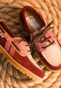 Paire de chaussures décontractées en daim rouge et rose avec lacets marron sur fond de corde beige épaisse, une chaussure montrant le nom de marque CAVAL à l’intérieur.