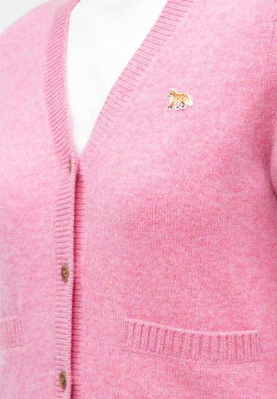 Cardigan roz din lână, cu decolteu în V, margini cu nervuri și două buzunare frontale. Prezintă un mic logo brodat cu un animal pe partea stângă.