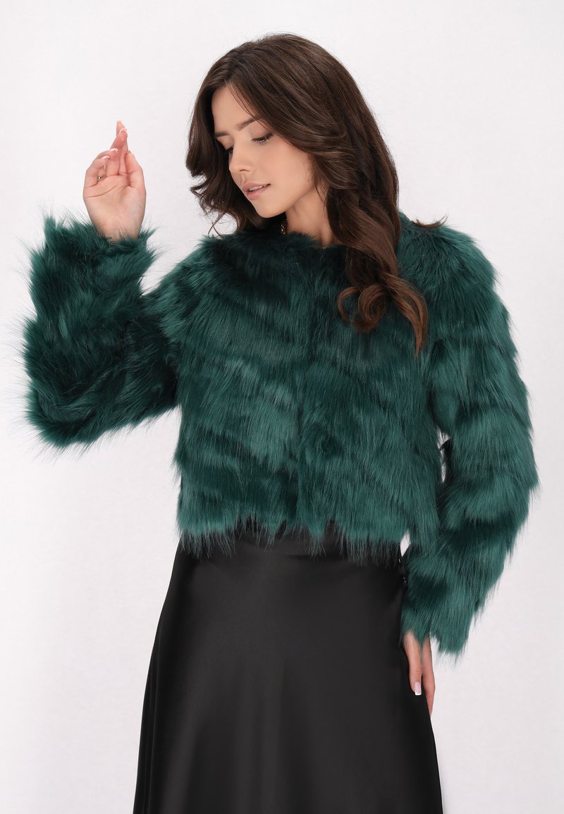 Jachetă scurtă din blană sintetică de culoare teal, cu mâneci lungi, având o textură moale și un guler rotund, asortată cu o fustă din satin negru.