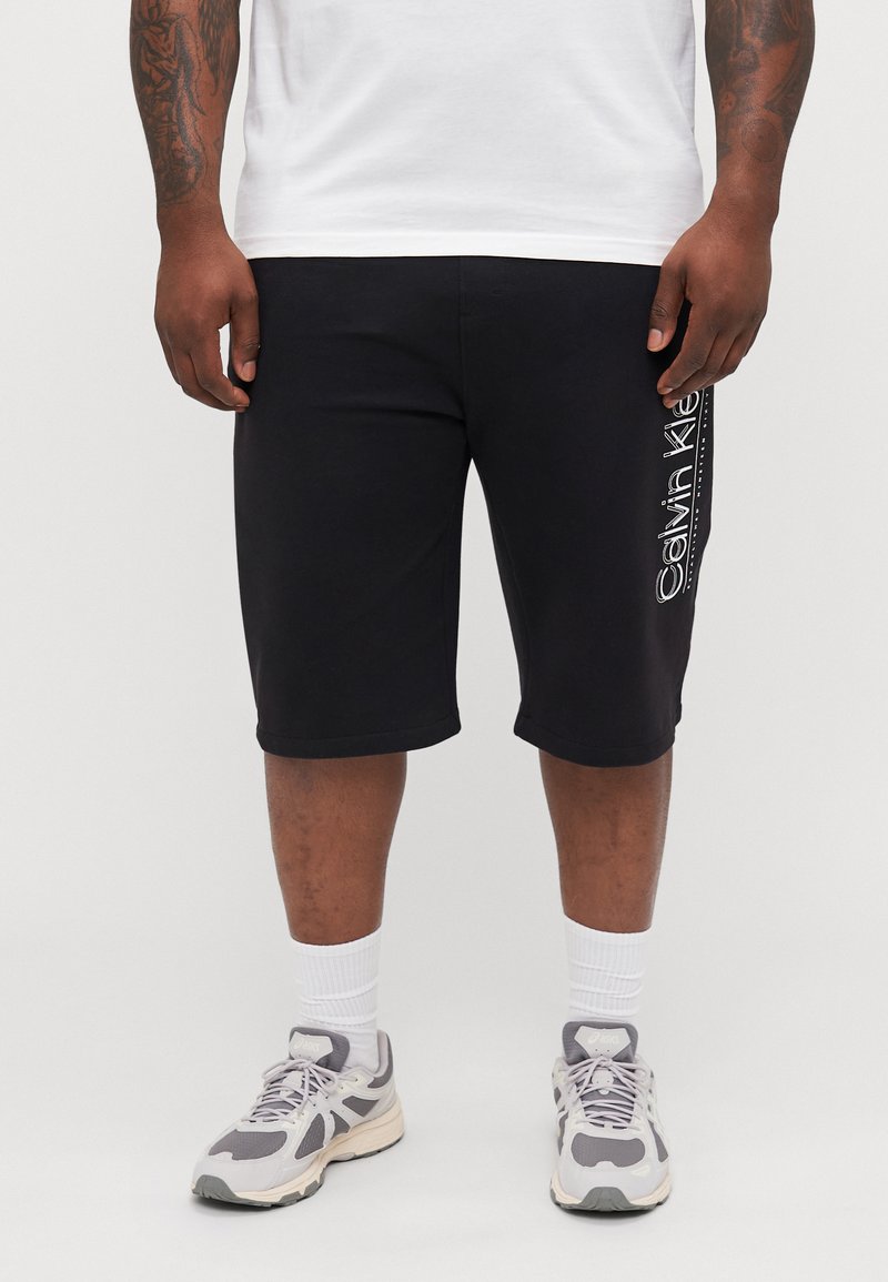 Svart bomullsshorts med avslappet passform, utstyrt med en hvit Calvin Klein-logo på siden, og avsluttet med rullede kanter.