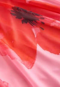 Lágyan omló anyag áttetsző textúrával, nagy piros virágmintákkal rózsaszín háttéren, lágy, réteges hatást keltve.