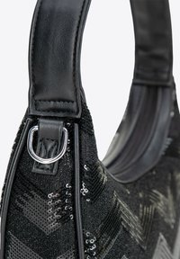 Borsa nera con una superficie testurizzata caratterizzata da motivi a zig zag in paillettes. Ha una tracolla in pelle liscia e dettagli in metallo.