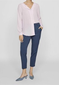 Blouse rose pâle à manches longues et col en V ; pantalon ajusté bleu marine ; escarpins bleu à enfiler. Tissu lisse avec un design épuré.