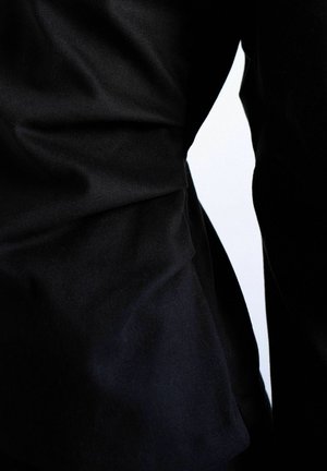 Plis et plis de tissu noir sur un fond blanc, mettant en valeur la texture et le contraste entre les zones claires et sombres.