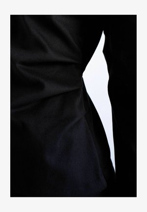 Plis et plis de tissu noir sur un fond blanc, mettant en valeur la texture et le contraste entre les zones claires et sombres.