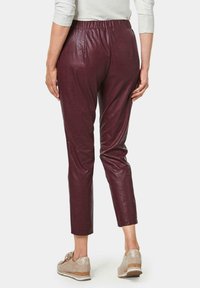 Bordeaux faux leren broek met een rekbare tailleband, slim fit en cropped lengte, gecombineerd met lichtgekleurde veterschoenen.