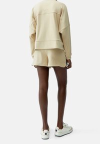 Conjunto de ropa de salón beige que incluye un sudadera de corte relajado y pantalones cortos. Textura suave con tonos apagados, mostrando un diseño minimalista y detalles de costura.