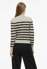 Turtlenecktröja i ljusgrått med svarta horisontella ränder, med långa ärmar och en kortad design. Bärs med svarta byxor.