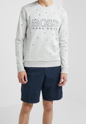 Grauer Sweatshirt mit dem Logo "BOSS HUGO BOSS" und verstreuten roten sowie marinefarbenen Akzenten. Gerippte Bündchen und Saum. Getragen mit marineblauen Shorts.