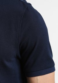 Camisa polo azul marino que muestra una tela texturizada, con mangas cortas y un primer plano del área del hombro y la parte superior del brazo.