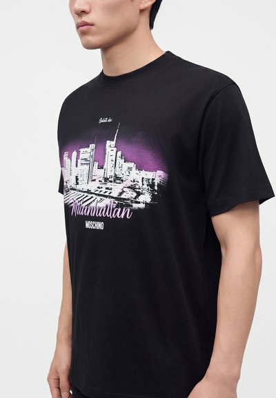 Homme portant un t-shirt noir avec une impression de skyline de ville blanche et violette et le texte "Milanhattan MOSCHINO" sur le devant.