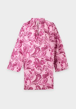 Mujer que lleva un vestido mini de manga larga con estampado rosa y morado, con escote en forma de olla y sandalias beige abiertas en los dedos.