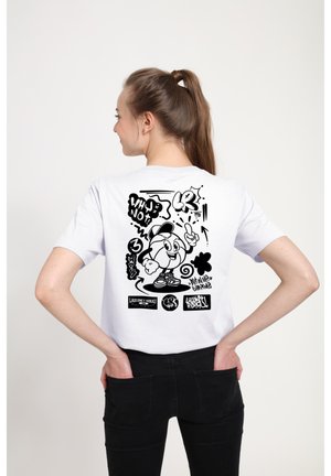 Kvinde med hestehale iført hvid skjorte med sort tegneseriefigur og graffiti-stil tekst og mønstre på ryggen.