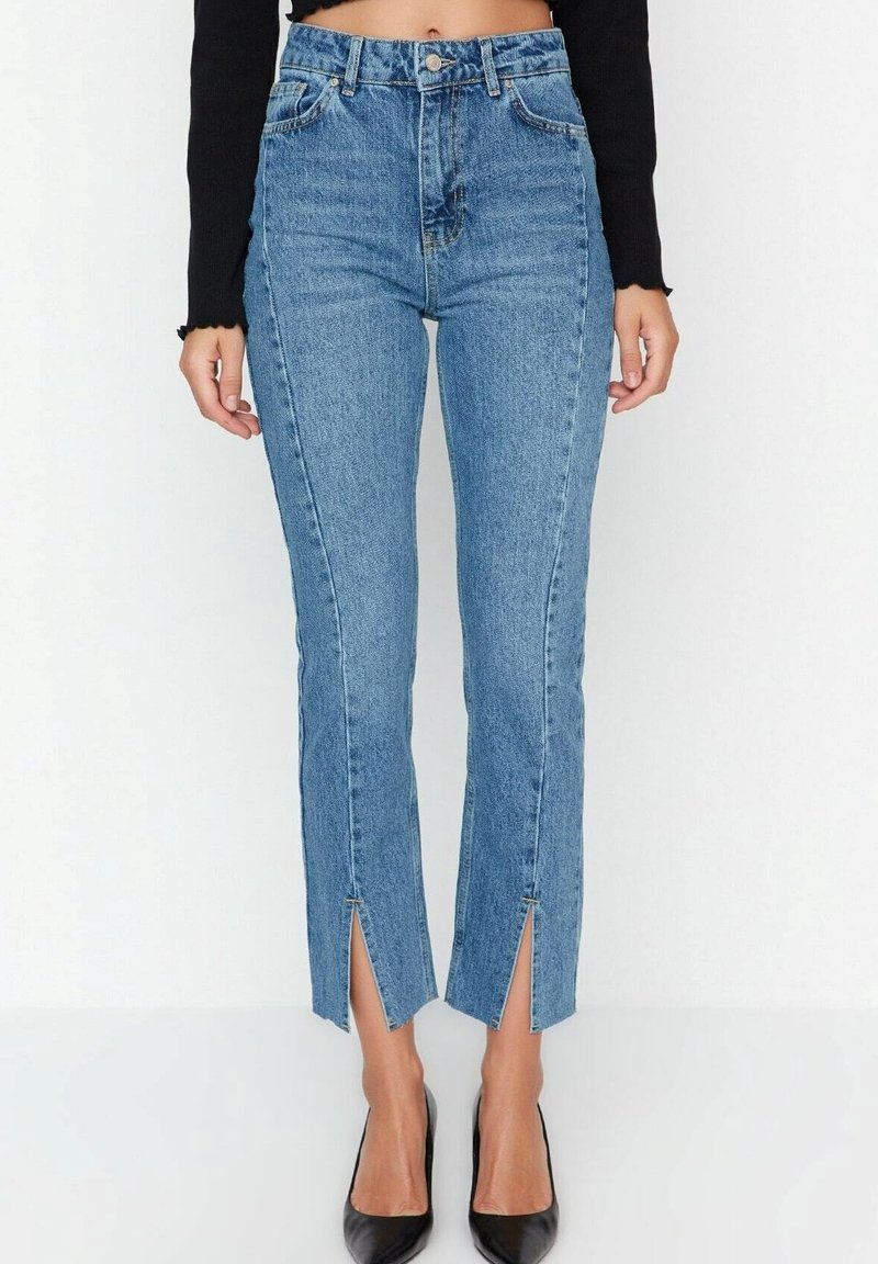Jeans en denim bleu taille haute avec une coupe slim, présentant des ourlets fendillés, un délavage clair et un design classique à cinq poches.