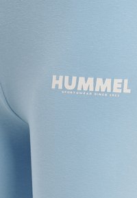 Ljusblå sporttyg med en slät textur. Har en vit tryckt logotyp "HUMMEL SPORTSWEAR SINCE 1923" på framsidan.