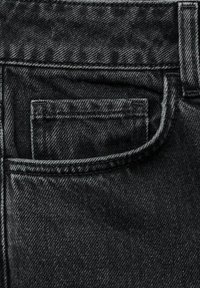 Acercamiento de unos jeans de mezclilla negra que muestran el bolsillo frontal y el bolsillo para monedas con detalles de costura visibles.