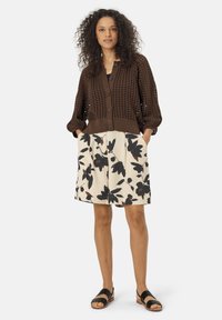 Cardigan en maille marron avec un devant à boutons et une texture perforée, associé à une jupe crème avec un imprimé floral noir. Sandales noires.