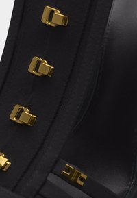 Κοντινή λήψη μαύρου δερμάτινου παπουτσιού με τετράγωνα καρφιά από κίτρινο μέταλλο στην ταινία.