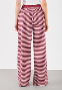 Wide-leg pants featuring a red and white striped pattern, elastic waistband, and soft fabric, shown from the back.