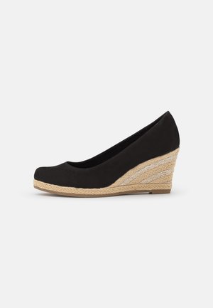 Zapato de cuña de ante negro con punta redonda y detalles trenzados de yute en el tacón. Textura suave y ligera elevación en la parte posterior.