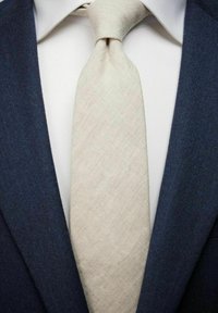 Vaaleanbeige-solmio, jossa on hienovarainen rakenne, solmittuna kauluksessa, yhdistettynä tummansiniseen pukuun. Sen alla on valkoinen paita.