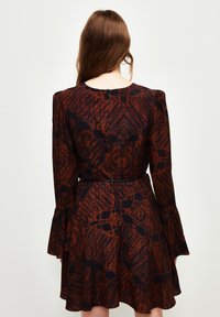 Braun gemustertes Kleid mit langen Ärmeln, schwingenden Manschetten und tailliertem Schnitt. Verfügt über einen runden Ausschnitt und einen Reißverschluss auf der Rückseite.