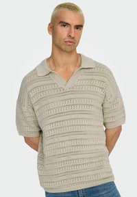 Beige polo shirt met korte mouwen, voorzien van een textuur gebreid patroon, met een V-hals en een brede ribbenkraag. Casual ontwerp met een losse fit.