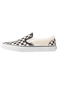 Zapatilla slip-on a rayas en blanco y negro con parte superior de lona, acentos elásticos en los laterales, suela de goma blanca y etiqueta de marca en el costado.