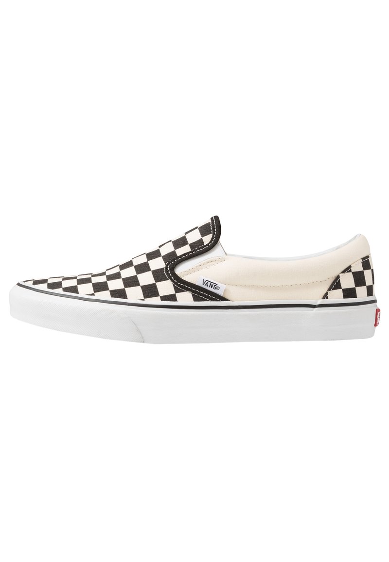 Zapatilla slip-on a rayas en blanco y negro con parte superior de lona, acentos elásticos en los laterales, suela de goma blanca y etiqueta de marca en el costado.