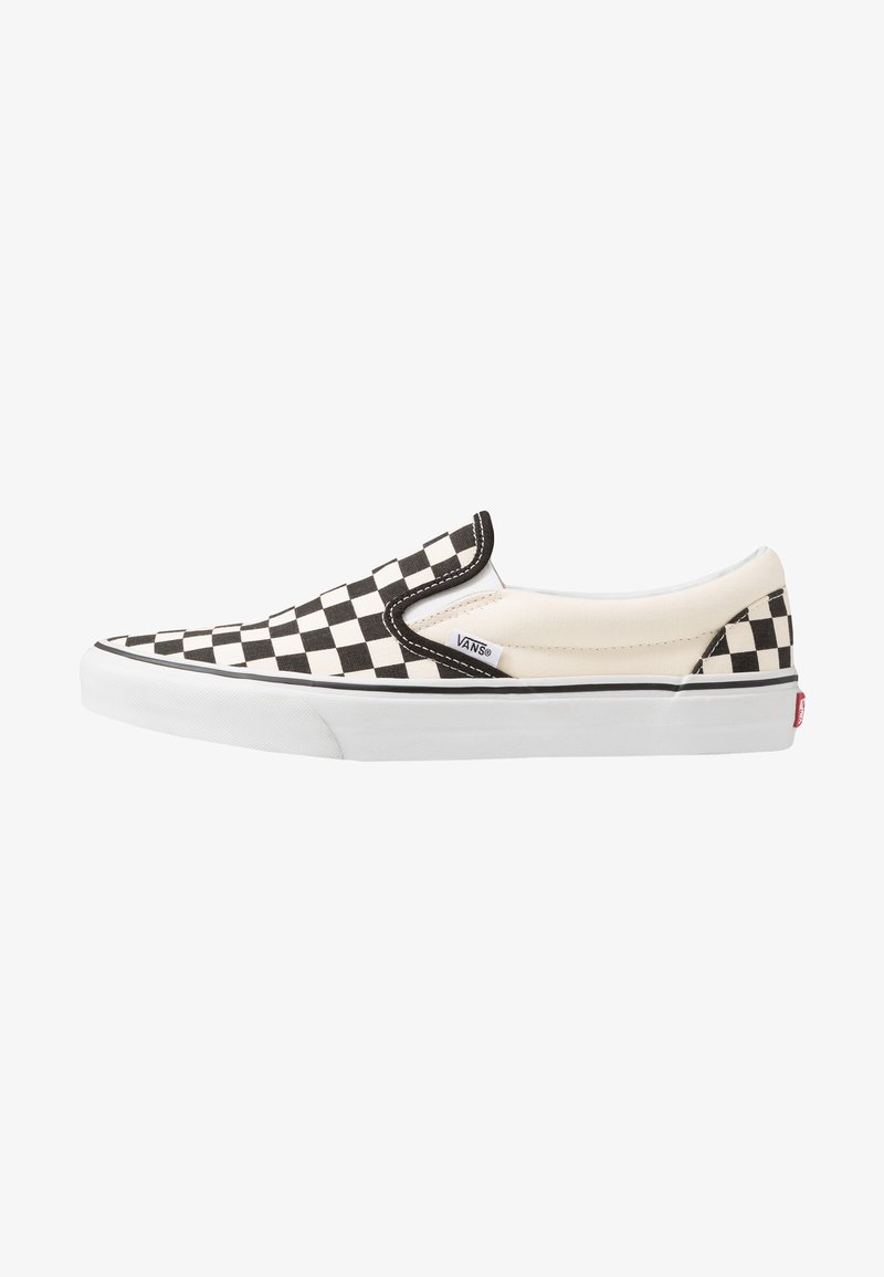 Zapatilla slip-on a rayas en blanco y negro con parte superior de lona, acentos elásticos en los laterales, suela de goma blanca y etiqueta de marca en el costado.