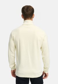 Chemise à manches longues jaune clair avec un col haut, présentant une texture côtelée. Le dos affiche un design uni avec des détails de couture minimaux.