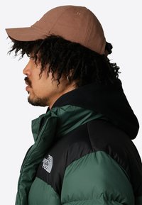 Chaqueta acolchada verde y negra con un alto cuello y cierre de cremallera. Gorra marrón con visera estructurada y orificios de ventilación. Tejido texturizado.