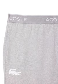 Svetlosiva tkanina s sivim elastičnim pasom, na katerem je delno napisan napis "LACOSTE" in bel krokodilji logotip blizu spodnjega levega kota.