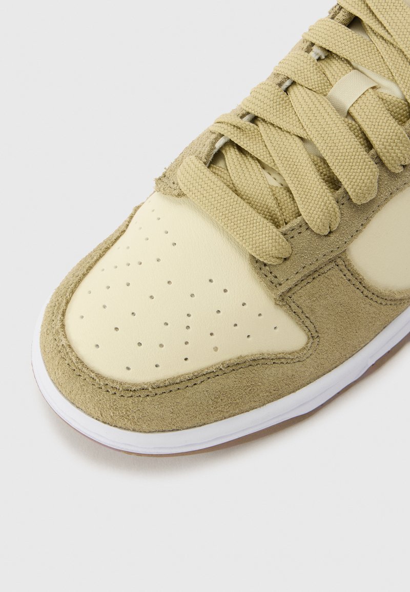 Sneaker en daim vert et cuir crème avec des perforations sur la boîte à orteils, des lacets plats et une semelle en caoutchouc blanc.