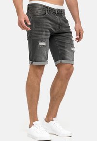 Shorts de denim negro con detalles deshilachados y dobladillos enrollados, con un diseño clásico de cinco bolsillos. Lleva deportivas blancas.