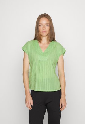 Blusa de manga curta em verde claro, com decote em V, apresentando riscas verticais e um corte ligeiramente descontraído. Usada com calças pretas.