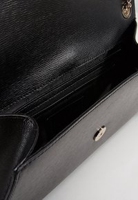 Borsa a mano in pelle nera con esterno testurizzato, dotata di chiusura a scatto in metallo dorato e molteplici scomparti interni per l'organizzazione.