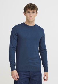 Pulover tricotat bleumarin, cu gât circular, mâneci lungi și manșete cu margine ondulată. Fabricat dintr-un material texturat, cu o formă ajustată.
